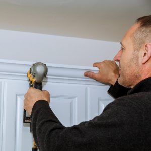 Handyman using brad nail gun on installation crown moulding wall kitchen cabinets trim
